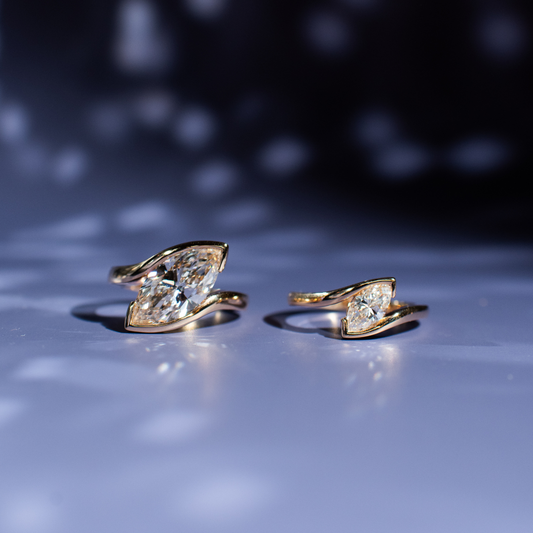 Two marquise diamonds set in solitaire bands on purple background