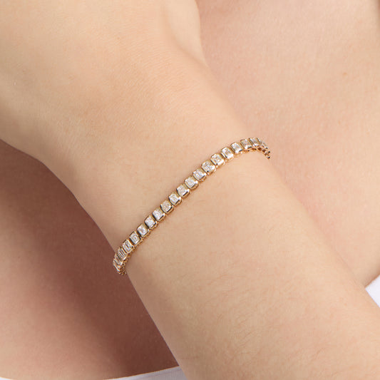 A yellow gold tennis bracelet with bezel set, emerald-cut natural diamonds on model wrist shot. 