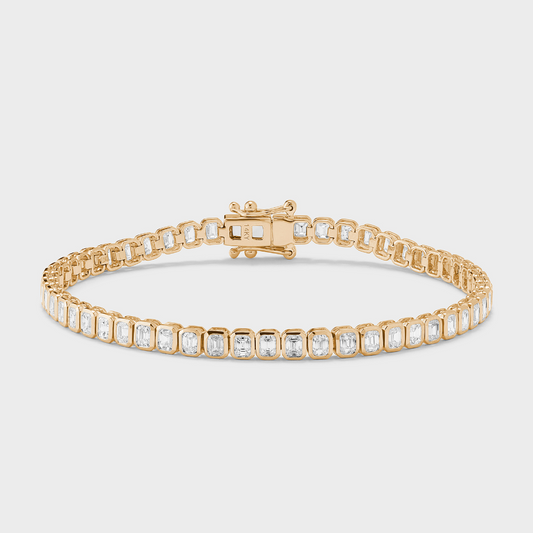 A yellow gold tennis bracelet with bezel set, emerald-cut natural diamonds against a white background. 