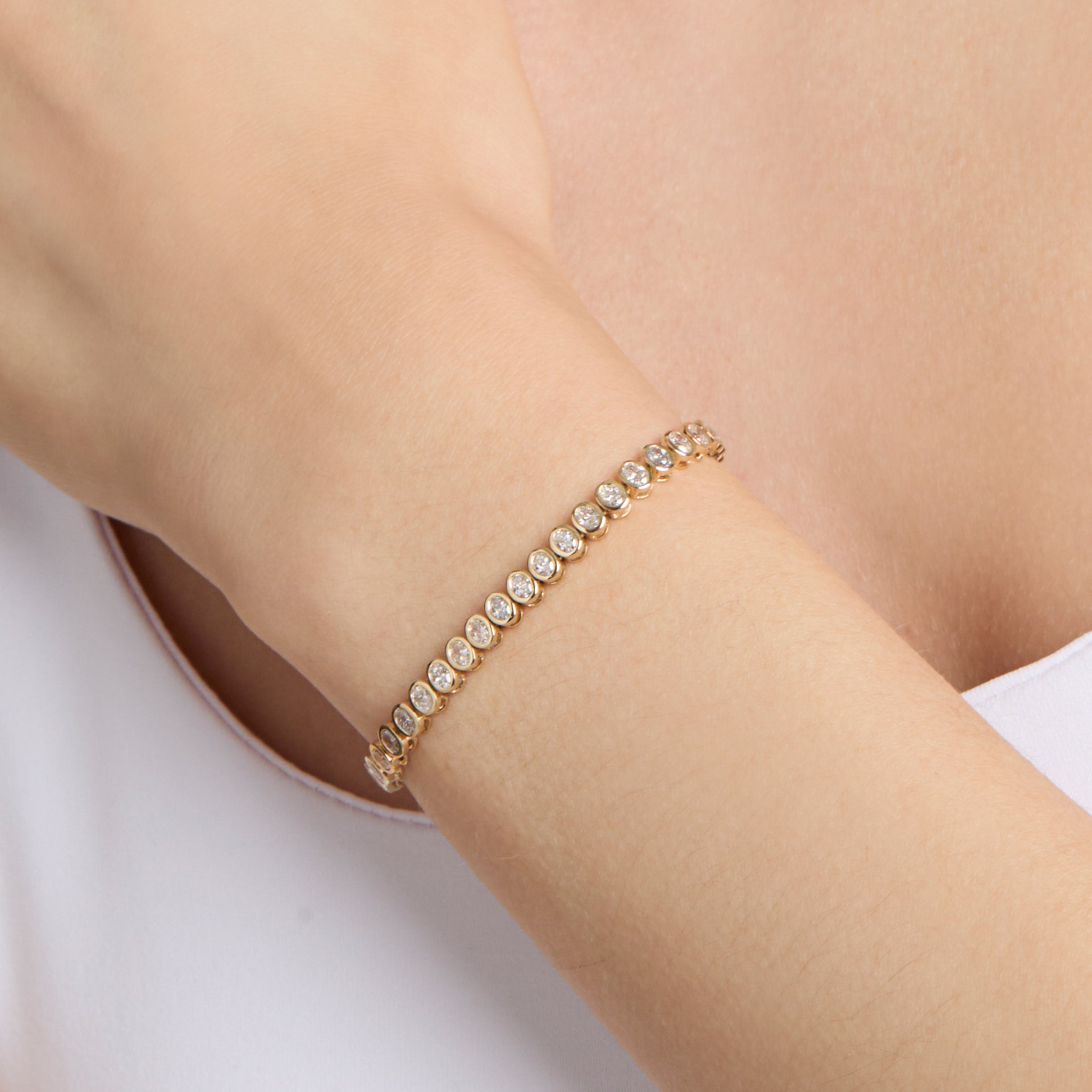 A yellow gold tennis bracelet with bezel set, oval shape natural diamonds on wrist
