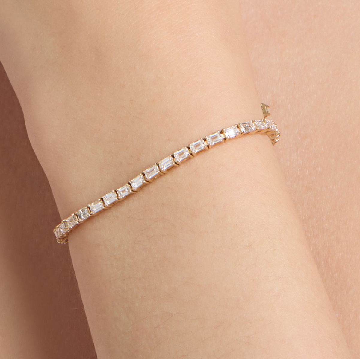 natural diamond tennis bracelet with emerald cut diamonds set east-west in yellow gold on wrist
