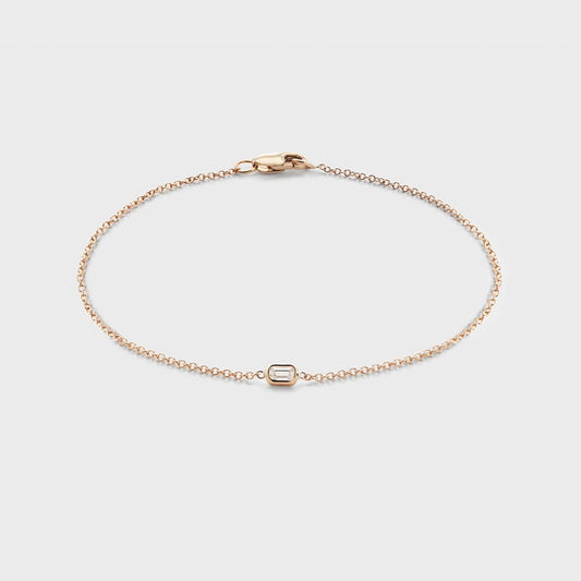 A yellow gold bracelet with a single bezel set baguette cut natural diamond. 