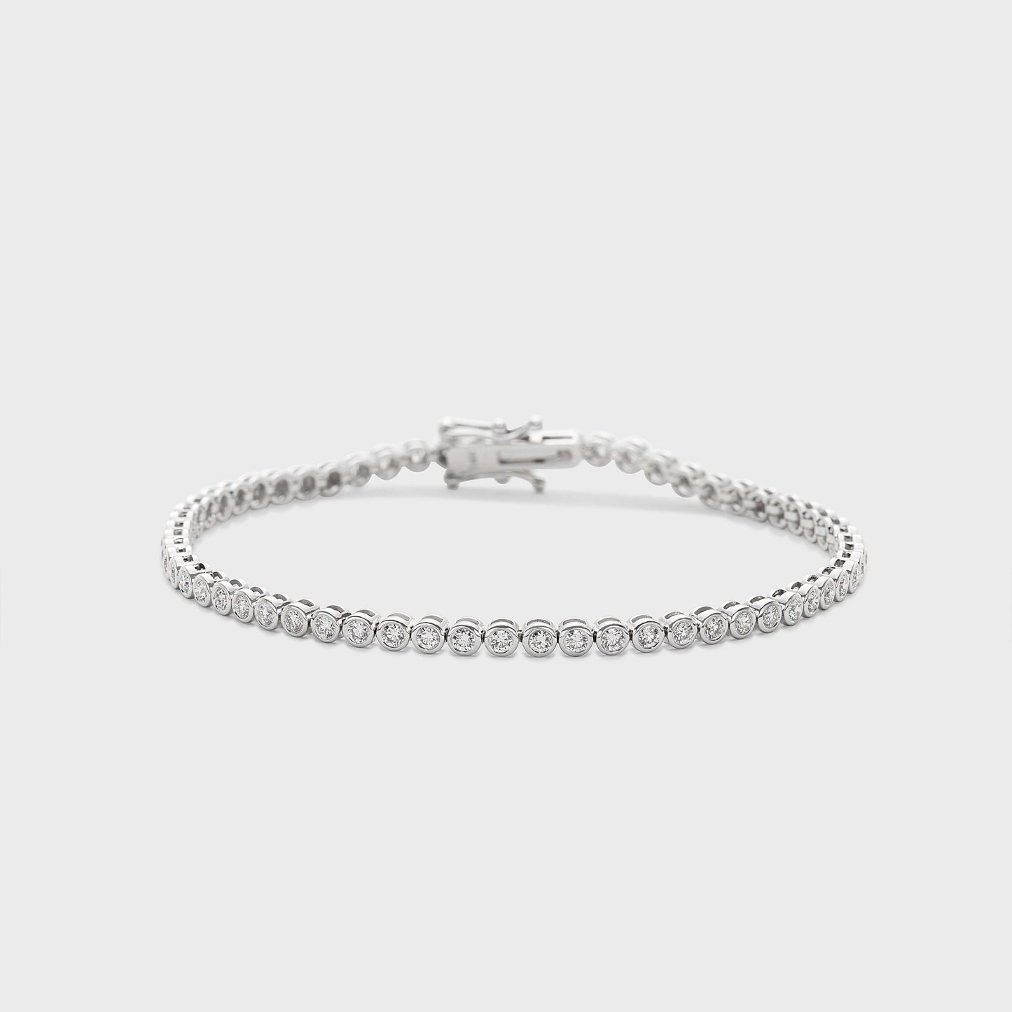 A white gold tennis bracelet with bezel set, round natural diamonds against a white background. 