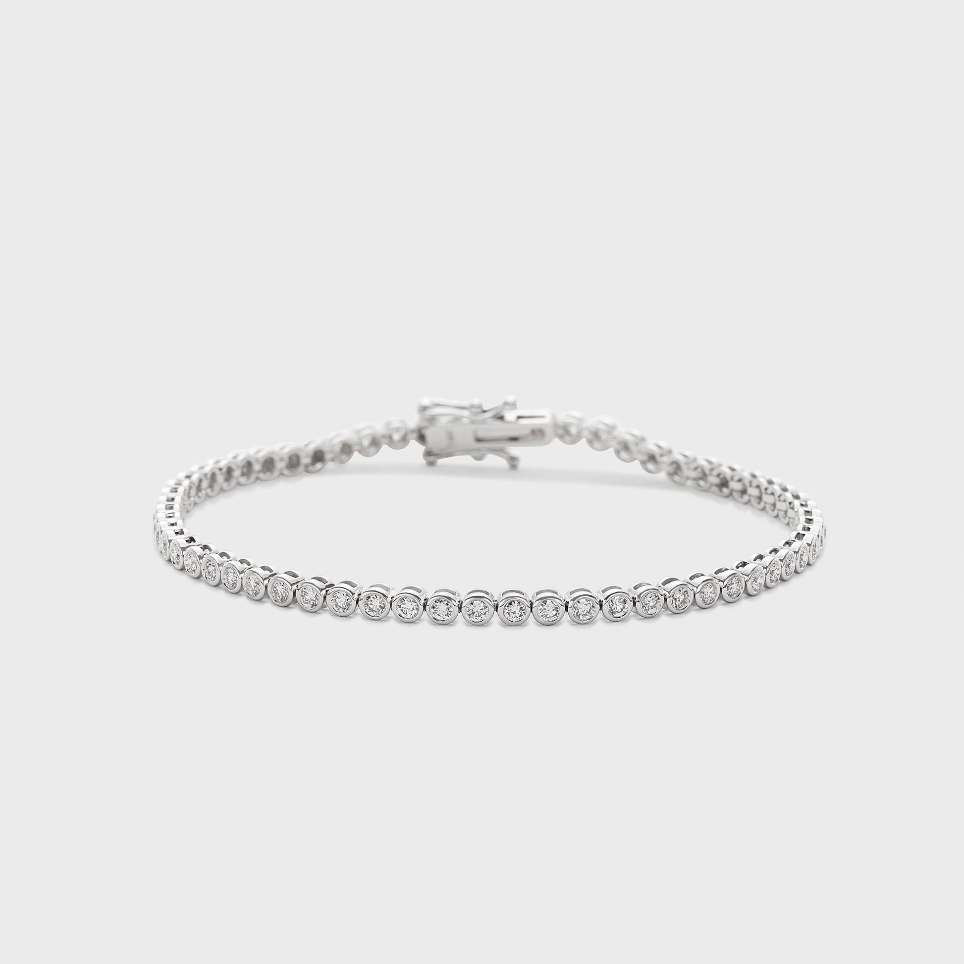 A white gold tennis bracelet with bezel set, round natural diamonds against a white background. 