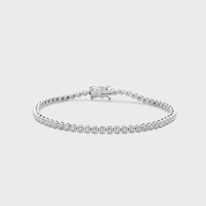 A white gold tennis bracelet with bezel set, round natural diamonds against a white background. 